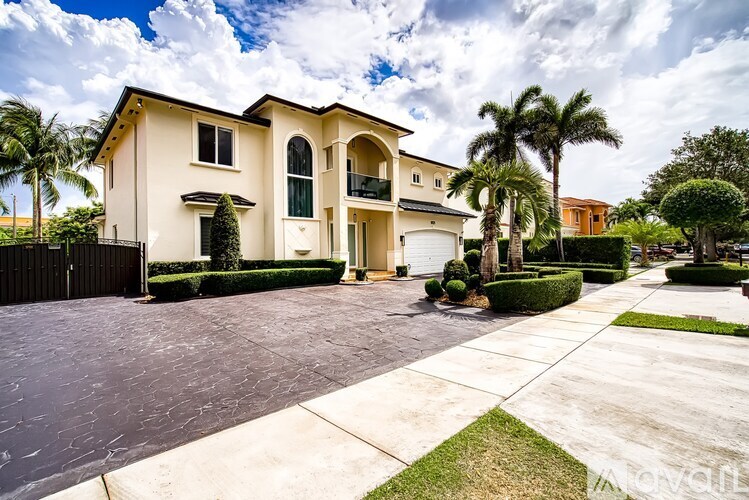 A large, two-story house with a driveway and palm trees in front.