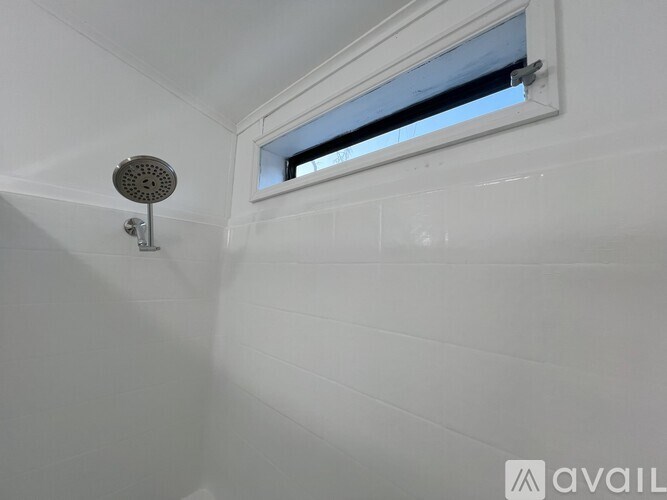 A white tiled bathroom with a window and a shower head.
