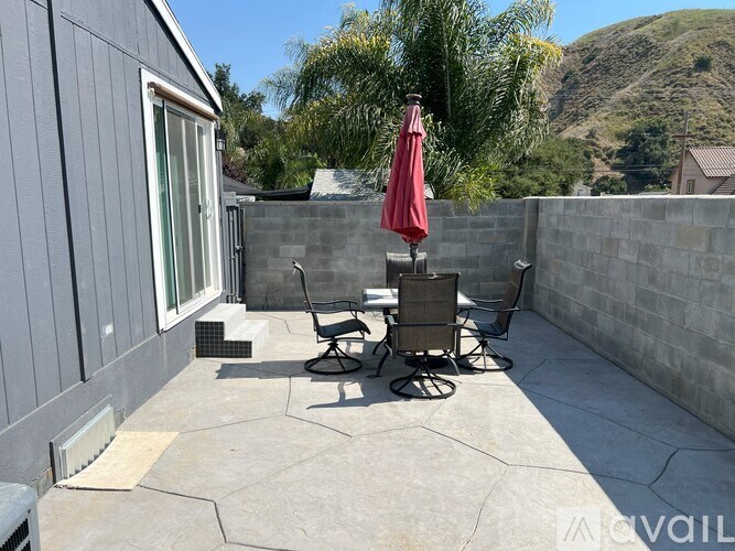 A patio with a table and chairs and a red umbrella.