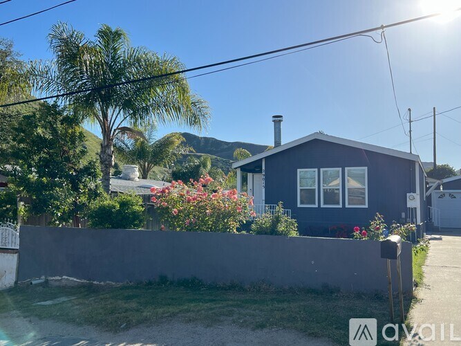 A house with a grey wall and a grey roof with a chimney and a mailbox in front of it.