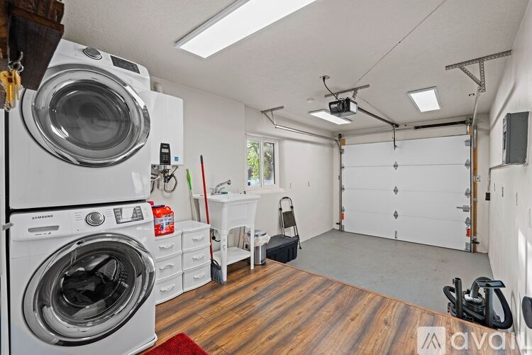 A laundry room with a washer and dryer, a red rug, and a white chair.