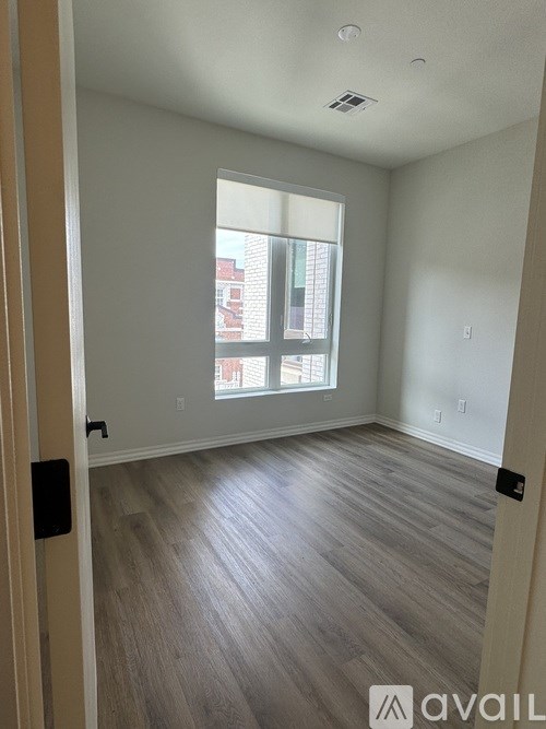 A room with wooden flooring and a window showing a red building outside.