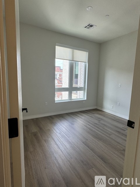 A room with wooden flooring and a window showing a red building outside.
