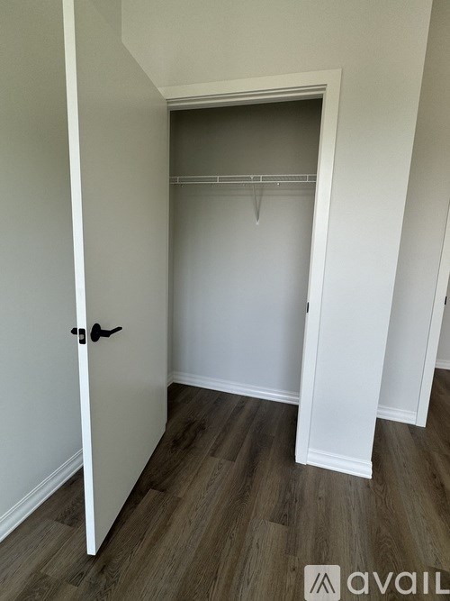A white door with a black handle is open to a white closet with a wooden floor.