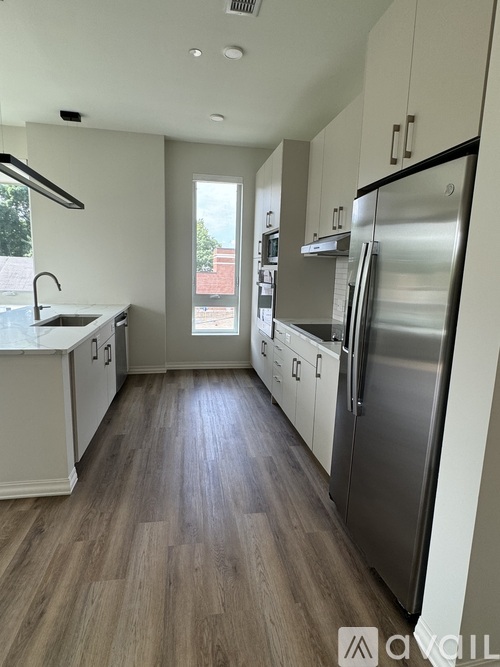 A kitchen with a refrigerator, sink, and wooden floors.