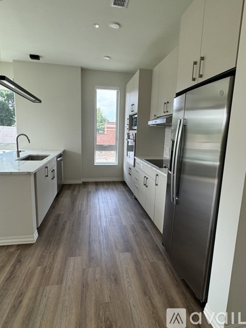 A kitchen with a refrigerator, sink, and wooden floors.