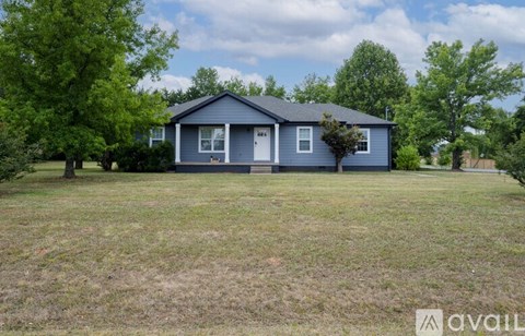 A blue house with a white door and windows is surrounded by green trees.