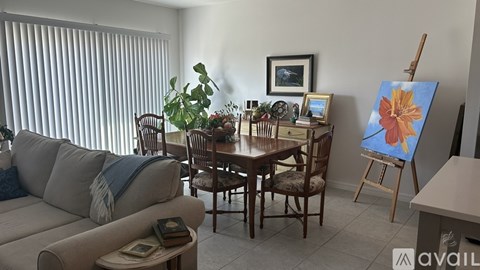 A living room with a couch, chairs, a table, and a painting on an easel.