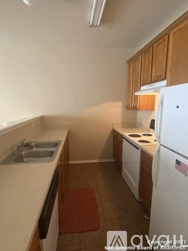A small kitchen with a white fridge and a red mat on the floor.