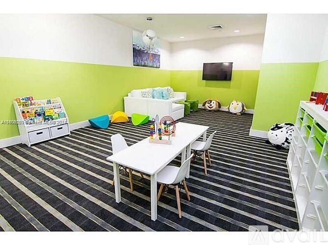 A room with a white table and chairs, a white sofa, a whiteboard, and a TV on the wall.