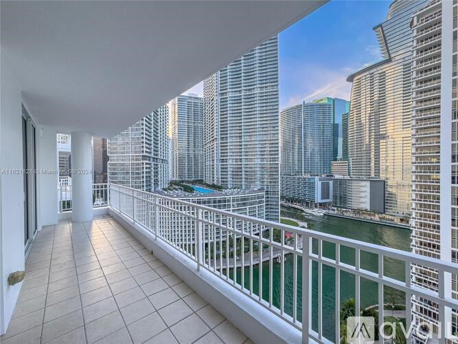 A balcony with a white railing overlooks a body of water with buildings in the background.