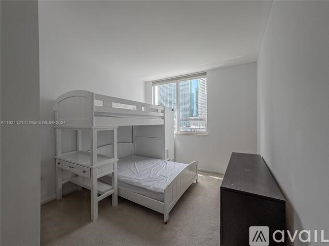 A white bunk bed with a desk underneath it in a room with a window.
