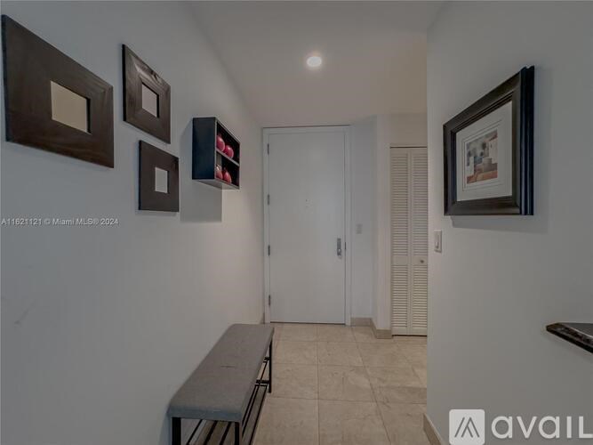 A hallway with a bench, pictures on the wall, and a door at the end.