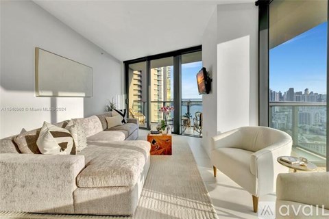 A living room with a white couch and a large window overlooking a city.