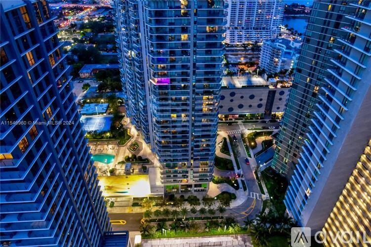 A cityscape at night with tall buildings and a lit-up street below.