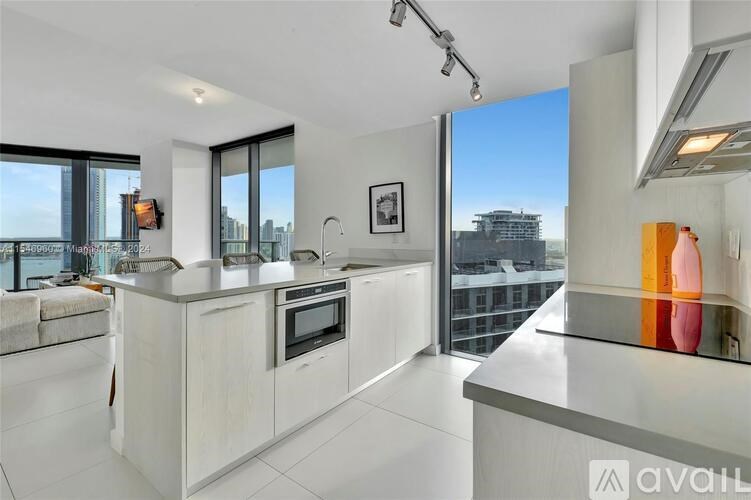 A modern kitchen with white cabinets and a large window overlooking the city.