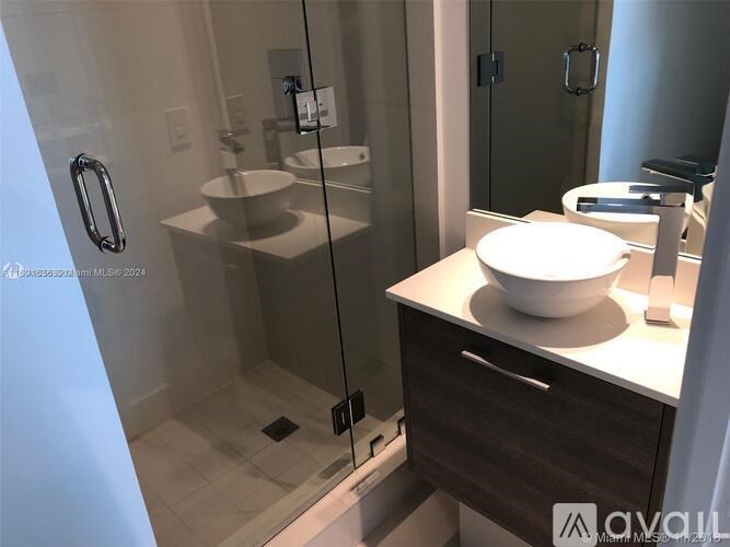 A modern bathroom with a glass shower stall and a white sink.