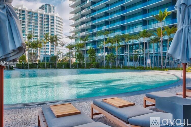 A pool area with sun loungers and umbrellas in front of a modern building.