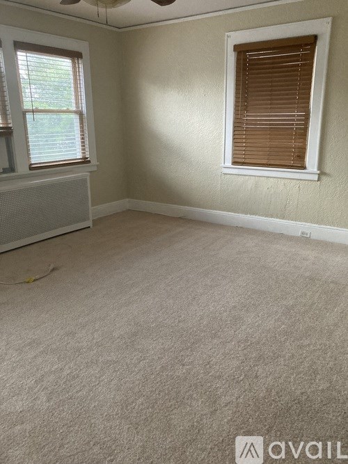 A room with a carpeted floor, a window with blinds, and a ceiling fan.