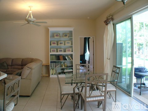 A living room with a glass table and chairs, a couch, and a ceiling fan.