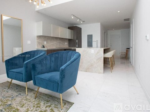 A blue velvet chair with gold legs is in the foreground of a modern kitchen.