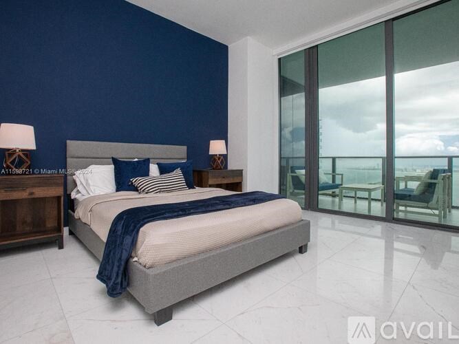 A bedroom with a bed, nightstand, and a view of the ocean.