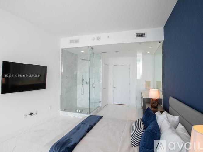 A bedroom with a bed, a lamp, and a TV mounted on the wall.