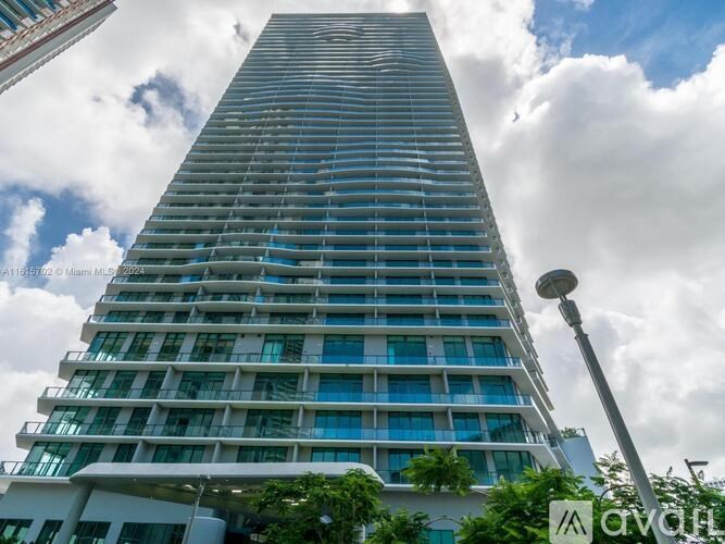 A tall building with many windows and balconies is seen against a cloudy sky.