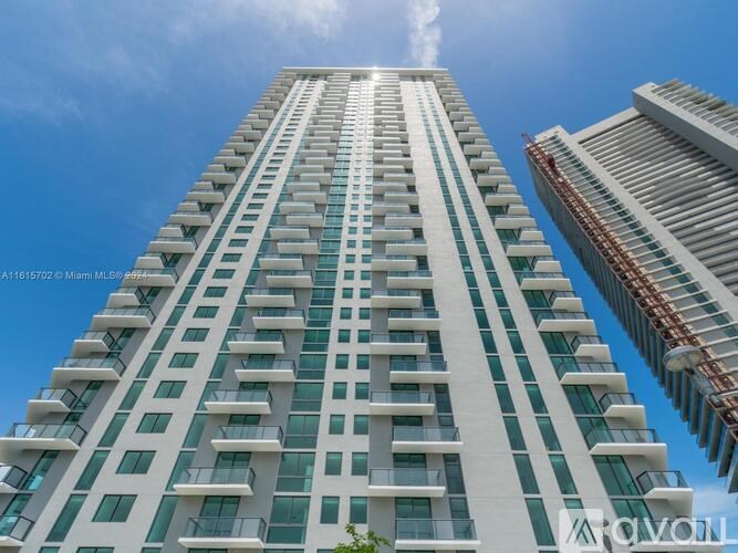 A tall white building with balconies is under a blue sky.
