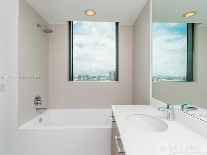 A white bathroom with a large window and a bathtub.