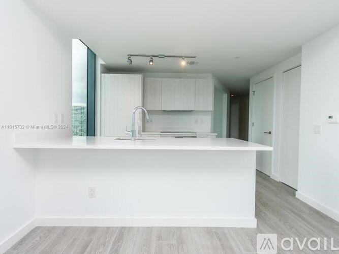 A modern kitchen with white cabinets and a wooden floor.