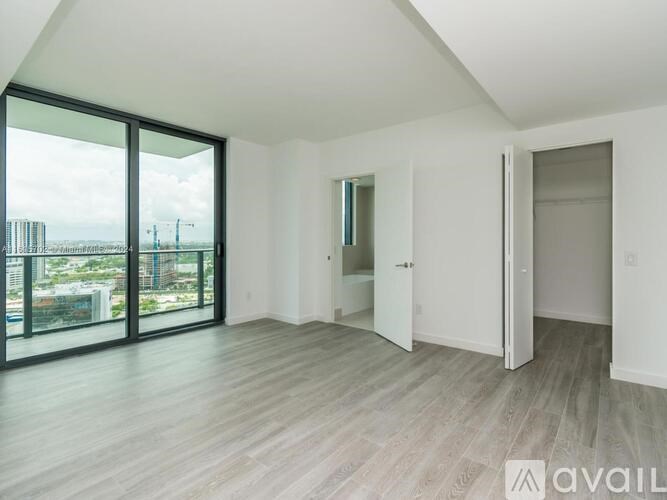 A spacious room with wooden flooring and large windows overlooking a cityscape.