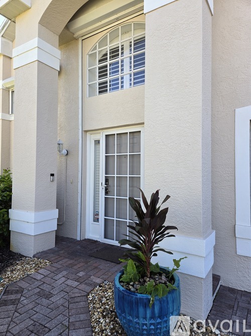 A plant in a blue pot sits on a brick walkway in front of a white door.