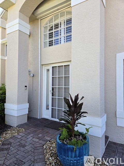 A plant in a blue pot sits on a brick walkway in front of a white door.