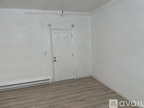 A room with a white door and wooden flooring.