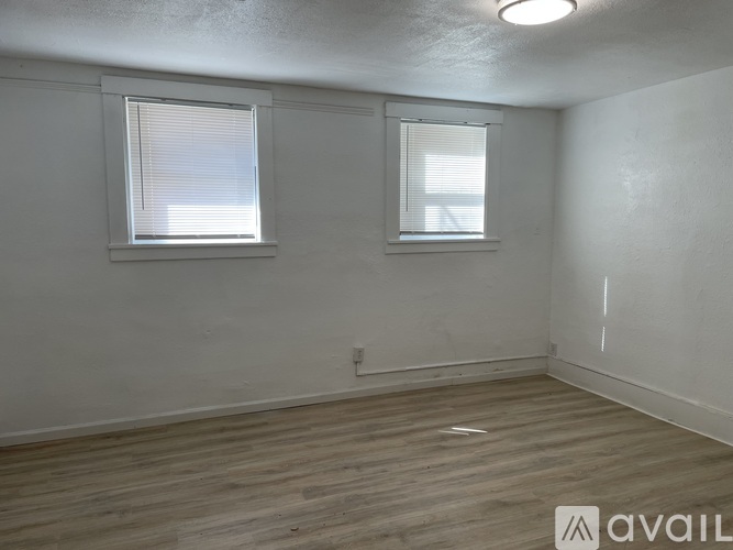 A room with wooden flooring and two windows.