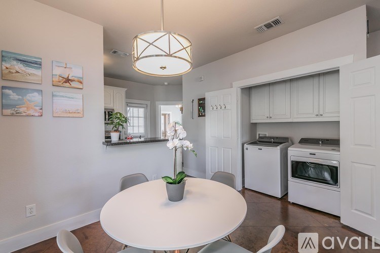 A white dining table with a plant on it and a kitchen in the background.