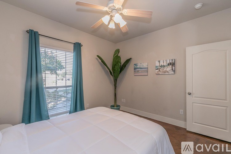 A bedroom with a bed, a ceiling fan, and a window with blue curtains.