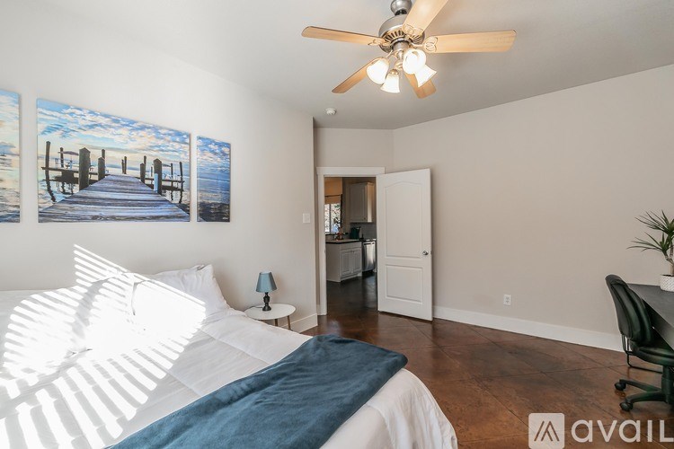A bedroom with a bed, a ceiling fan, and a painting on the wall.