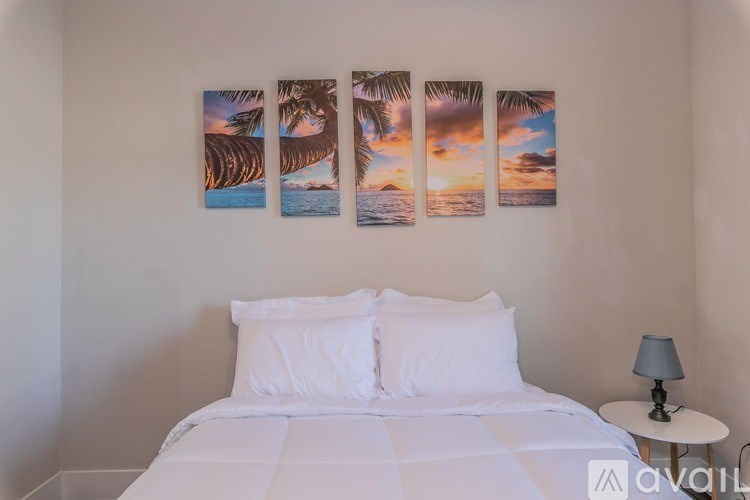 A bedroom with a bed, a lamp, and a wall with four pictures of palm trees.