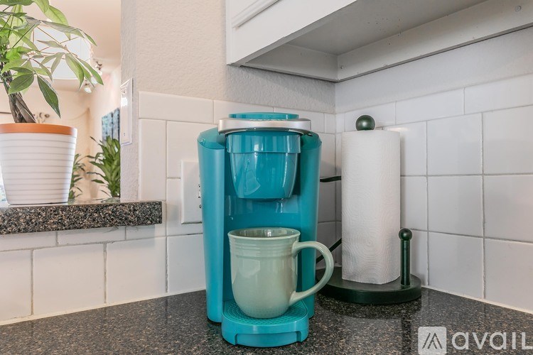 A blue coffee maker is on a counter next to a white container.
