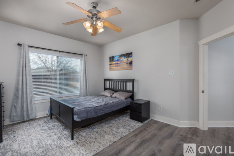 A bedroom with a bed, a ceiling fan, and a painting on the wall.