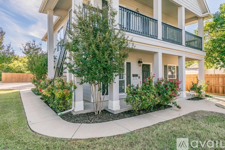 A white house with a balcony and a tree in front.
