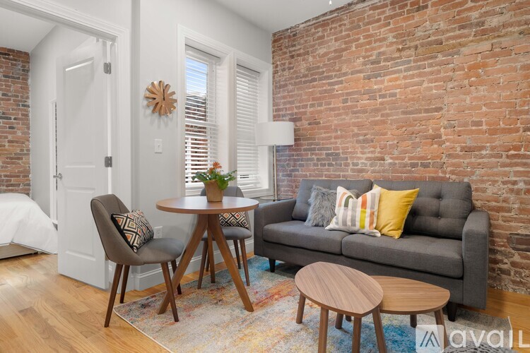A living room with a grey couch, a wooden table, and a brick wall.