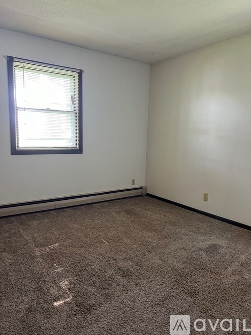 A room with a carpeted floor and a window with blinds.