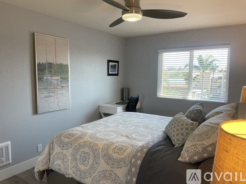 A bedroom with a bed, a ceiling fan, and a painting on the wall.