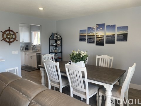 A dining room with a table set for four and a ship's wheel on the wall.