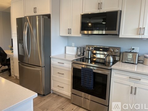A kitchen with a stainless steel refrigerator and oven, white cabinets, and a wooden floor.