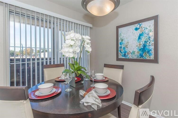A dining table set with plates and glasses is in front of a window with blinds.