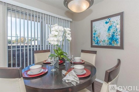 A dining table set with plates and glasses is in front of a window with blinds.